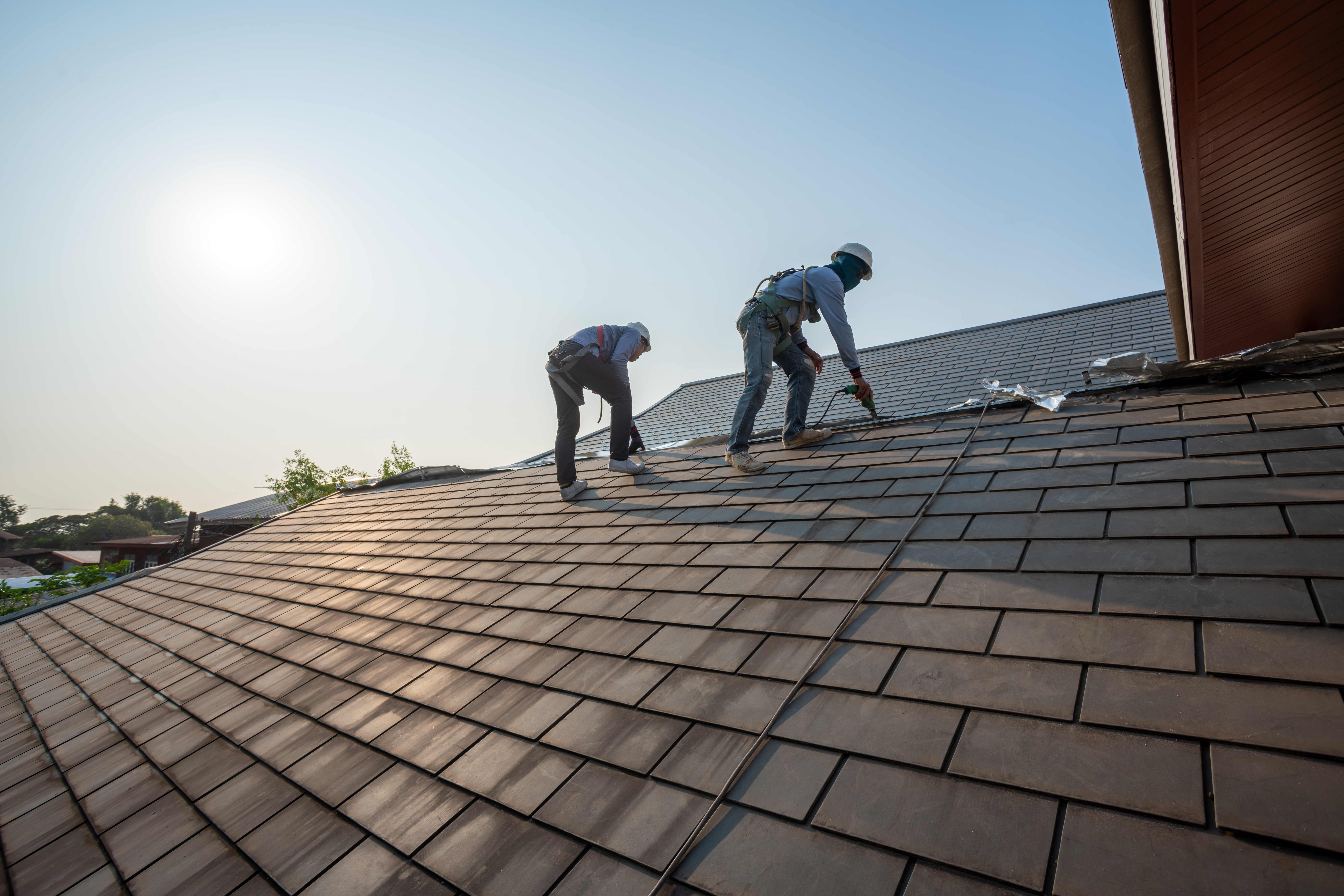 Roofer working in special protective work wear gloves, using air or pneumatic nail gun repair and replace roofing tiles on top of the new roof under construction residential building